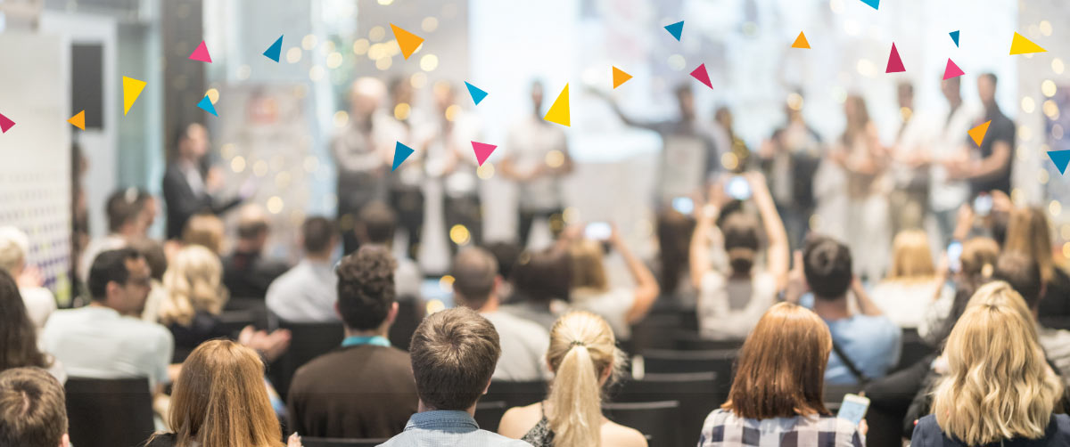 An audience looks on toward a stage of award recipients as colourful pixel illustrations float above their heads