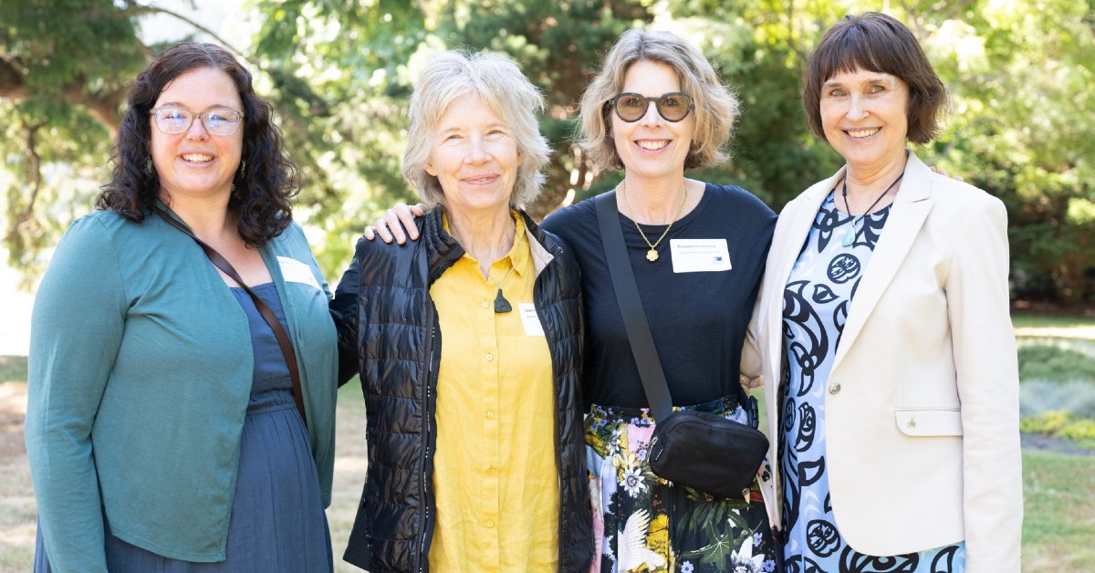 Susan Gee and three guests smile at the camera as they stand in front of a large tree 