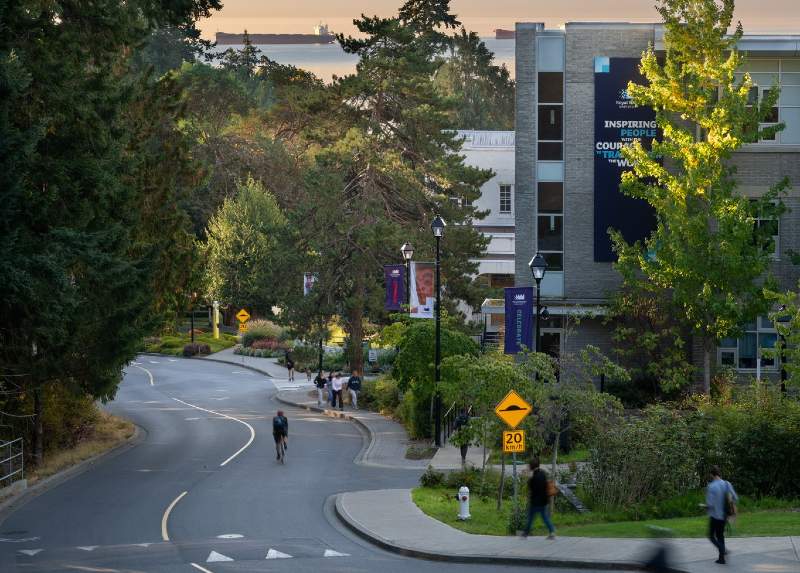 An aerial view of the RRU campus, looking down a winding road with people walking on the sidewalk, and buildings reflecting the light from dusk