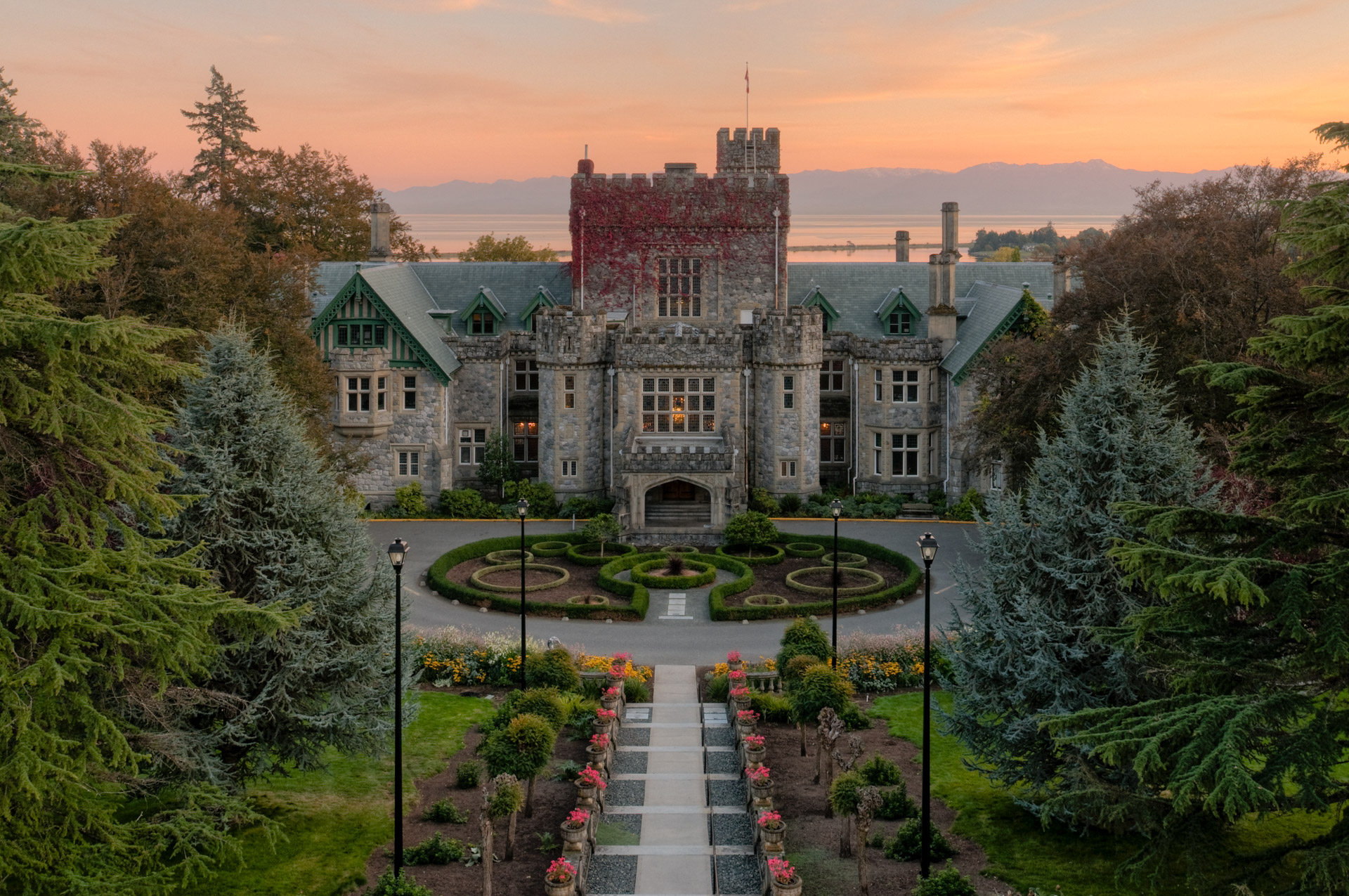 An aerial photo of Hatley Castle, set in front of the Olympic Mountains with green foliage surrounding it