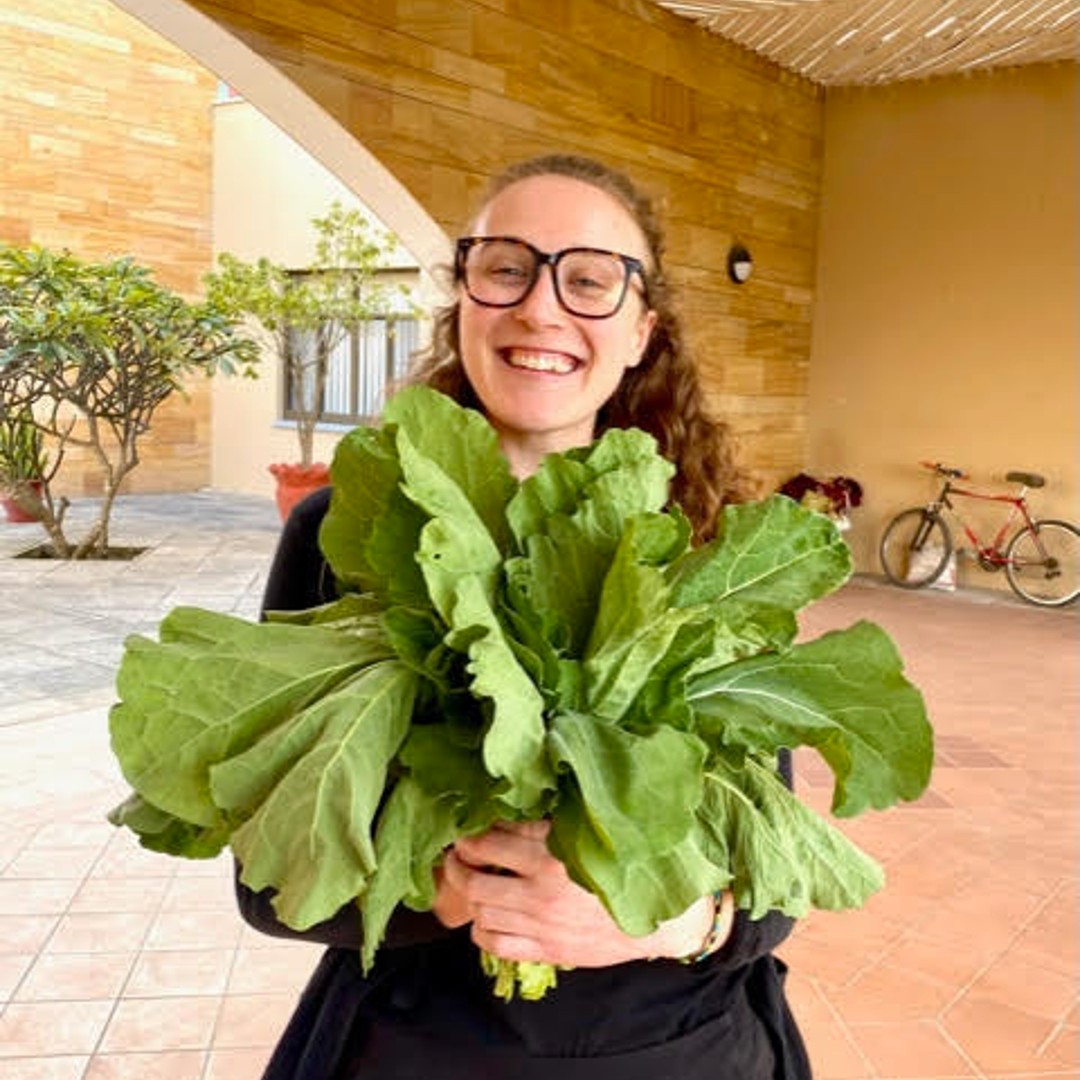 Emily Burkholder smiling and holding a large bouquet of leafy greens.