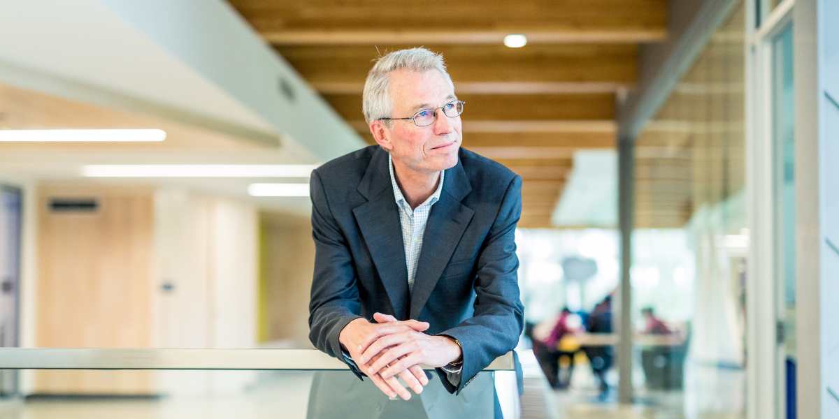 An RRU faculty member leans over a balcony indoors at the university looking onwards.