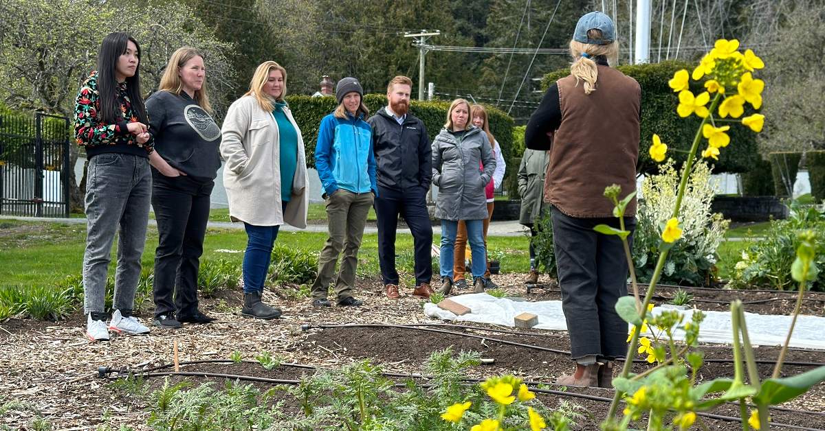 People standing in garden looking at a woman wearing a blue ballcap