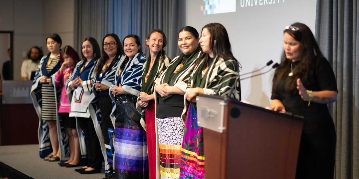 A group of Indigenous graduates stand on stage during their Convocation ceremony