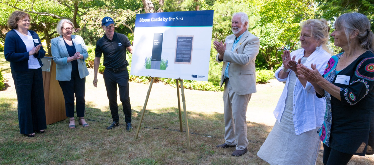 In a garden setting, people stand around a bristle board detailing a new gift to RRU.