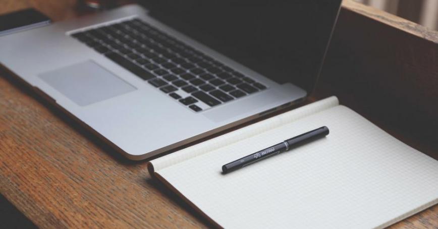 A laptop and notebook sitting on a wooden desk.