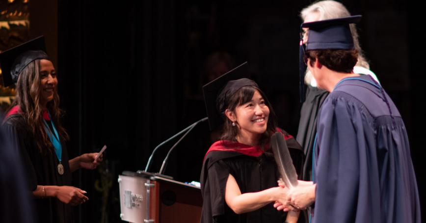 Graduate wearing academic regalia shakes hands on stage at Convocation.