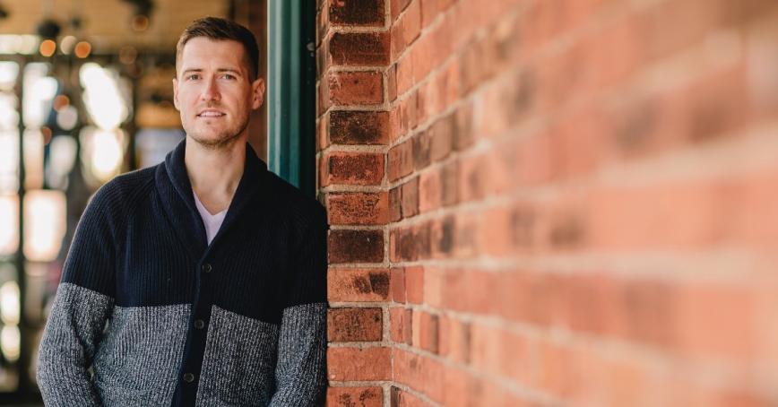 Matejs Kalns, Human Security and Peacebuilding grad, poses against brick wall.