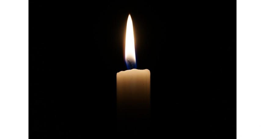 A lit white candle glows against a dark background