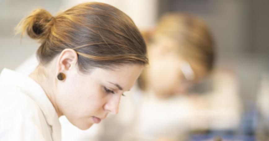 Student working in a lab coat next to a colleague