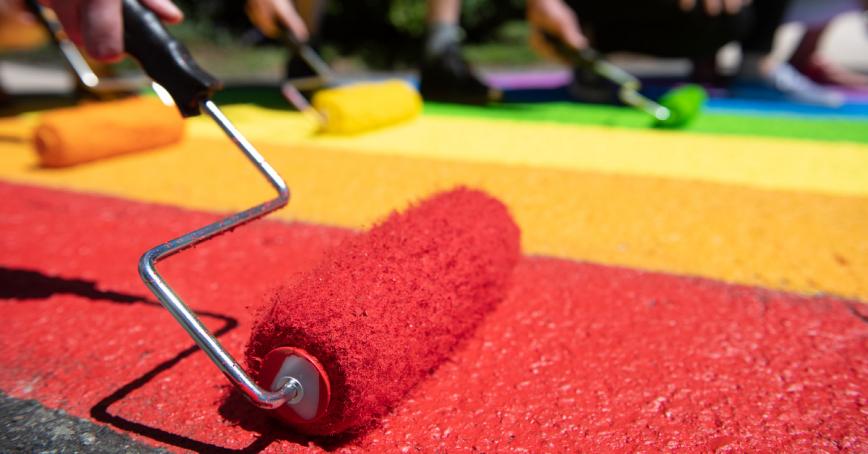 Paint rollers lined up in a row covering pavement in the Pride colours