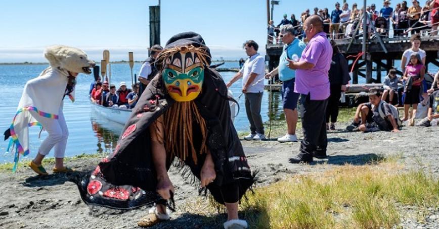 Indigenous dancers on beach at RRU with people looking on.