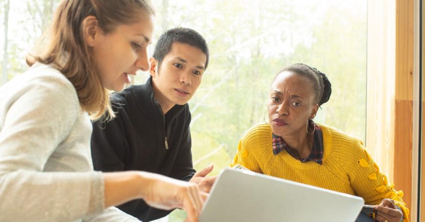 three students sitting in a row look at a laptop intently 