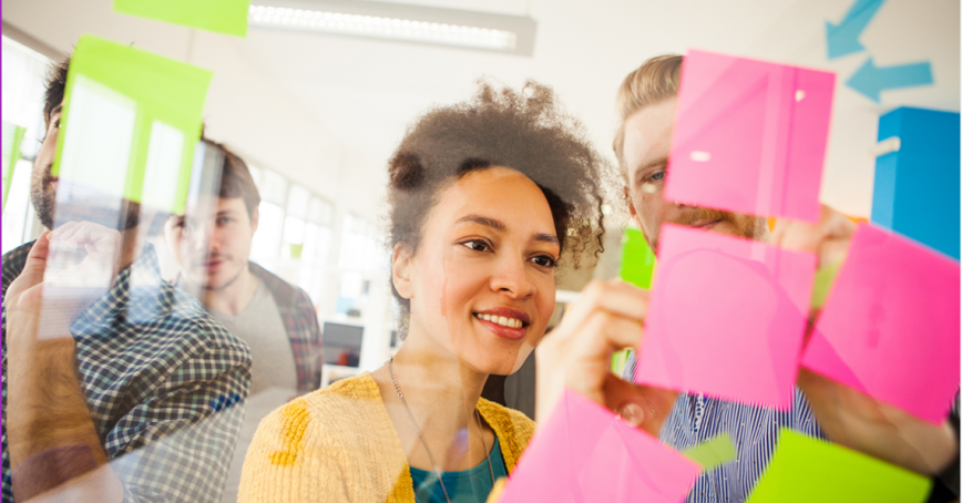 A group of educators brainstorm while writing on multi-coloured sticky notes pasted to a glass window.