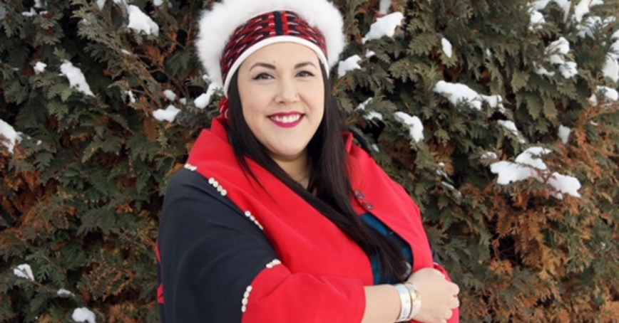 Juli Holloway is wrapped in a red and black blanket and wears a head piece. She looks happy.