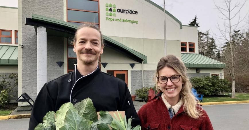 Chef Zeno and Solara Goldwynn stand outside Our Place with a box of fresh leeks and collards.