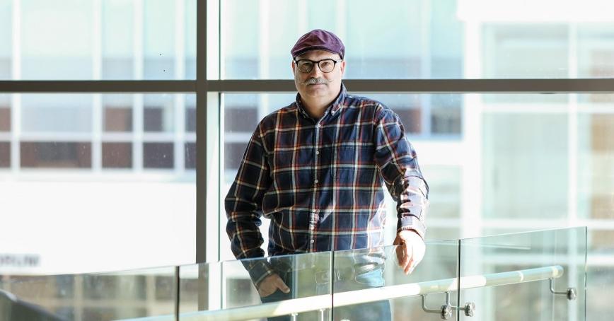 Man wearing hat and glasses standing in front of glass wall