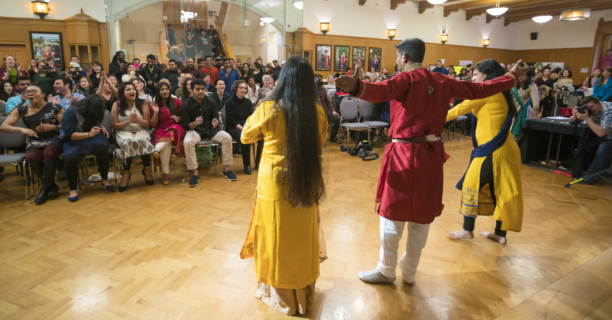 Three students in traditional cultural clothing dance in front of an audience of Royal Roads students and staff in the Grant Quarterdeck.