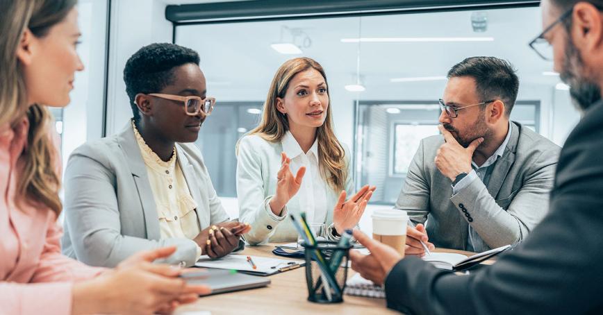 Five people in deep discussion around a conference table in an office setting.