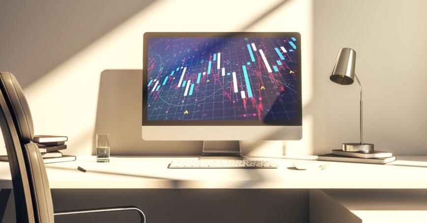 A computer with a line graph representing finances at an empty desk.