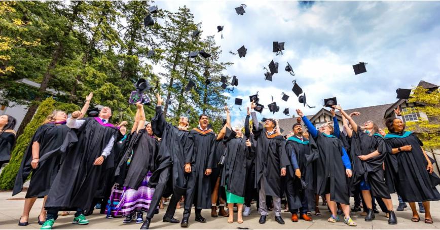 A group of Royal Roads students tosses their caps in front of the Sherman Jen Building