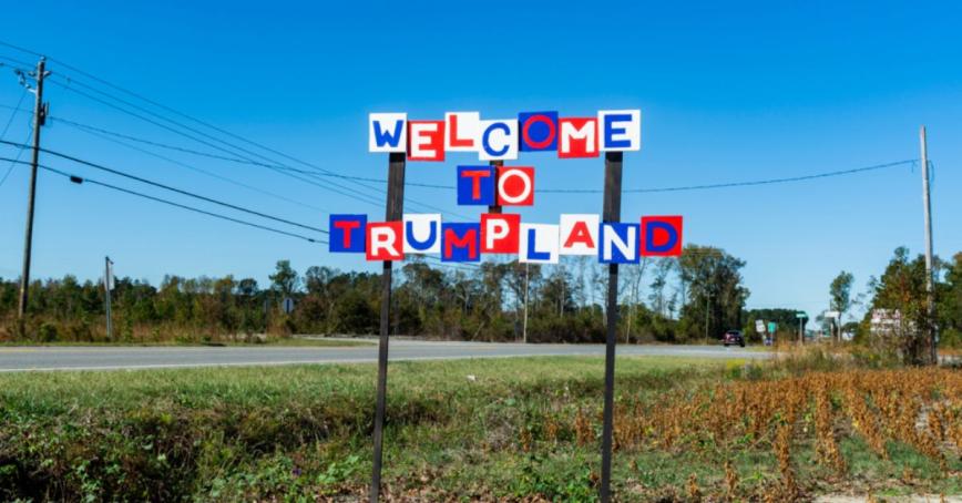 A sign that says "Welcome to Trump land" in front of a field