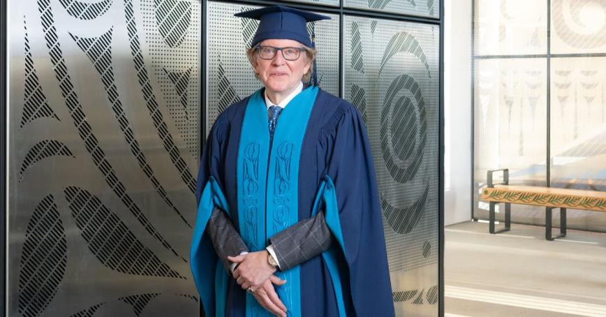 Anthony von Mandl stands in front of 'All my relations' art installation, wearing a cap and gown. 