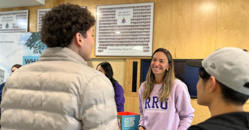 POV image over the shoulders of two high school students who are talking to a smiling RRU staffer wearing a lilac sweatshirt