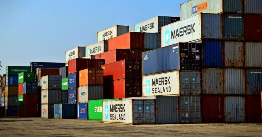 A variety of shipping containers are stacked up at a receiving yard. 