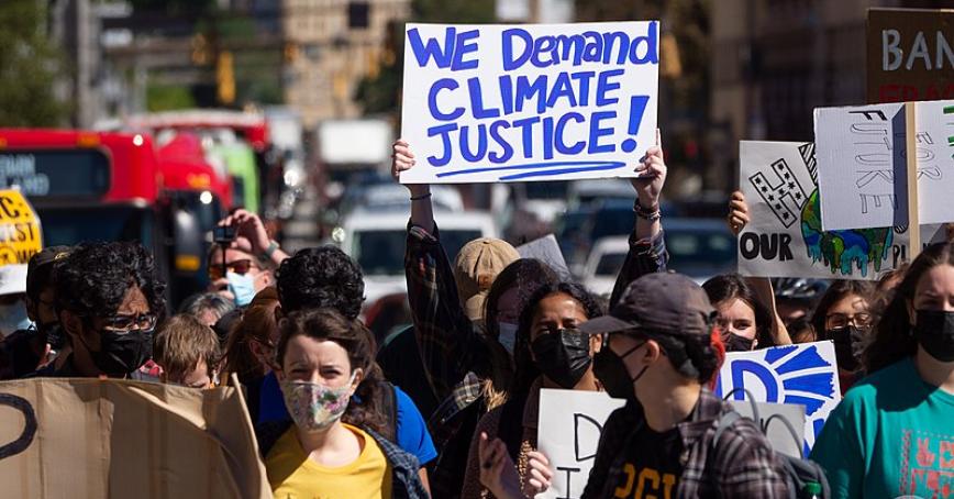 A group of protestors march, with a sign reading "We demand climate justice"