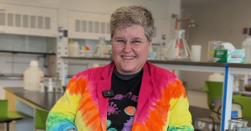 Dr. Mickie Noble smiles in this head shot in the science lab. She's wearing a tie dyed labcoat