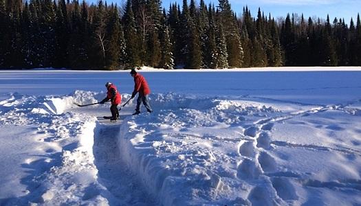 Two people playing hockey on a snow cleared frozen lake.