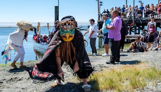 Indigenous dancers on beach at RRU with people looking on.