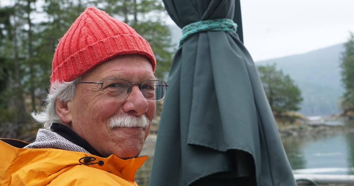 Richard Kool looking over his shoulder smiling next to a view of nature.