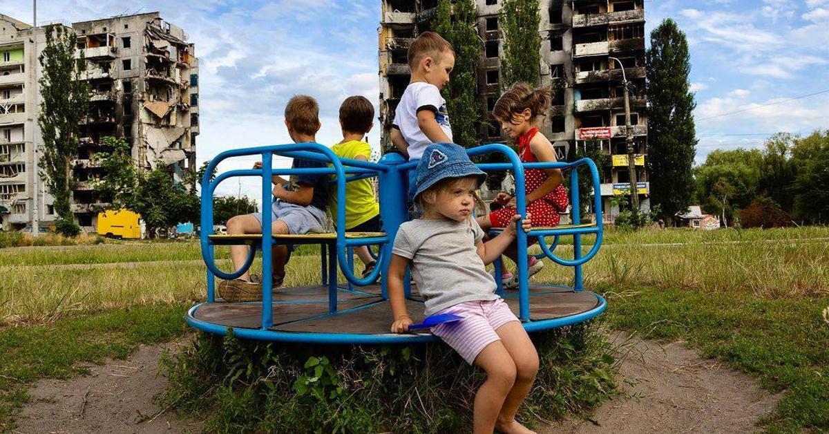 Ukrainian children sitting on playground equipment in war-torn territory