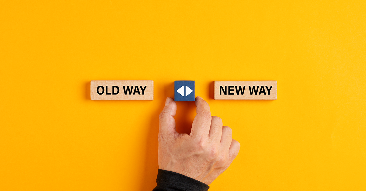 Male hand holds a wooden cube with arrow icon between the options of old way or new way.