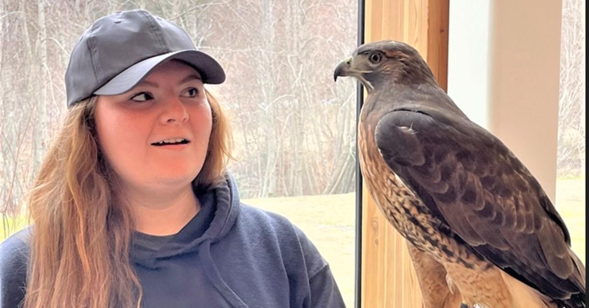 Student with a hawk perched on their arm standing in front of a glass window