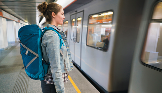 A person wearing a backpack stands on the platform near a passing trainn