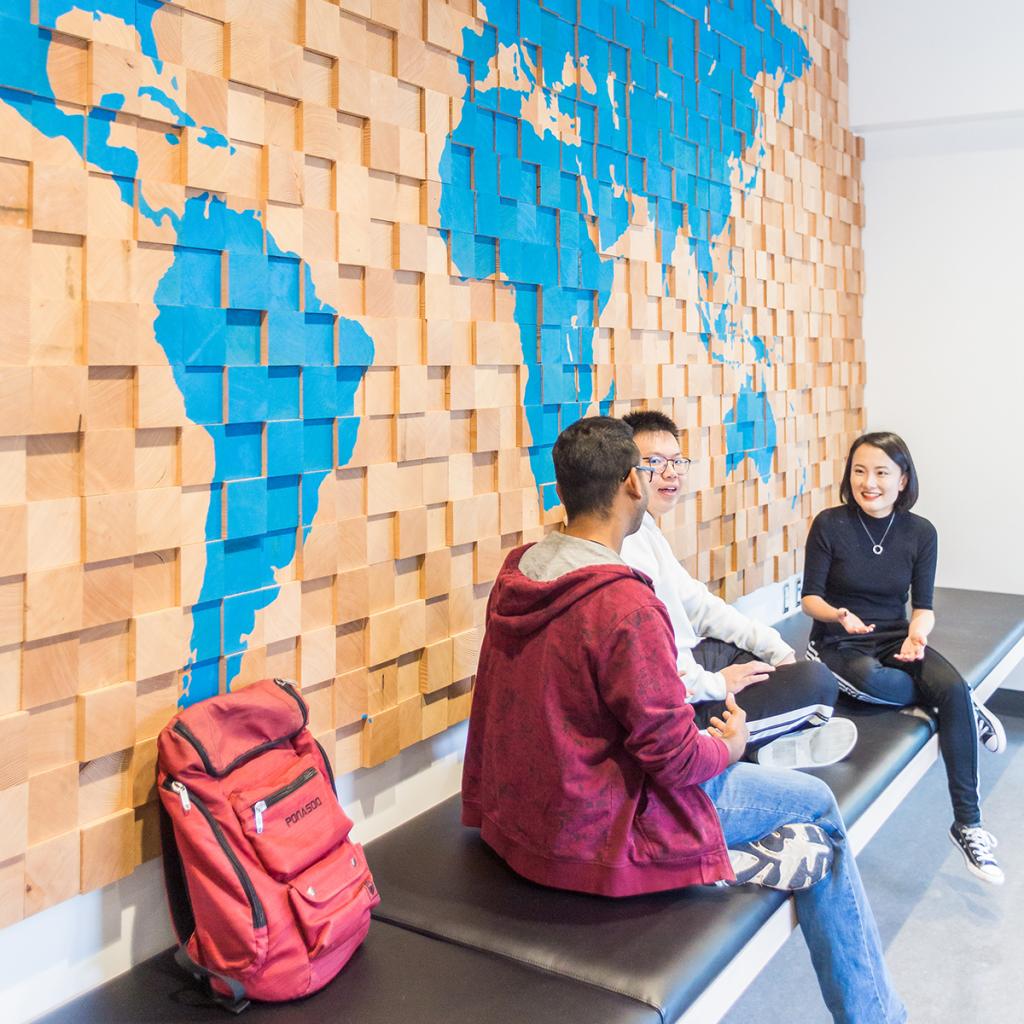 Three students sitting in front of artwork with world map