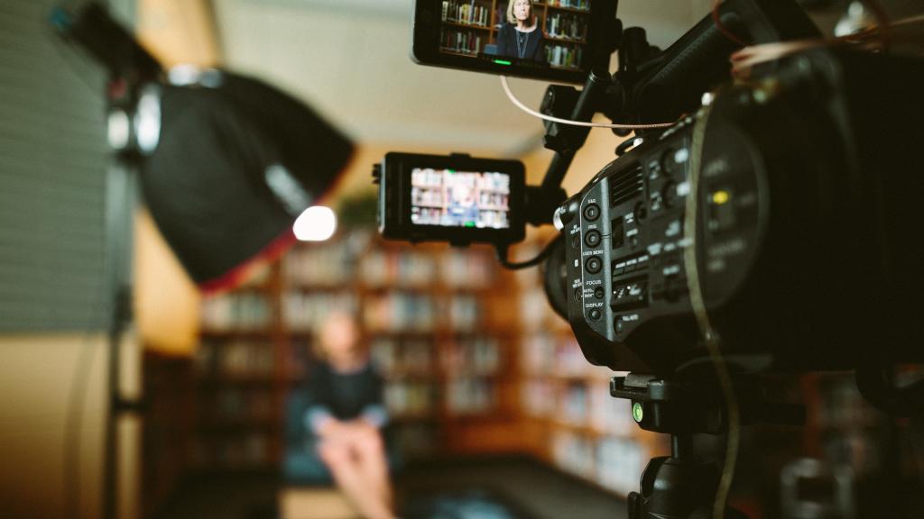 Video camera shooting an interview of someone in front of a wall of books. Image by Sam McGhee