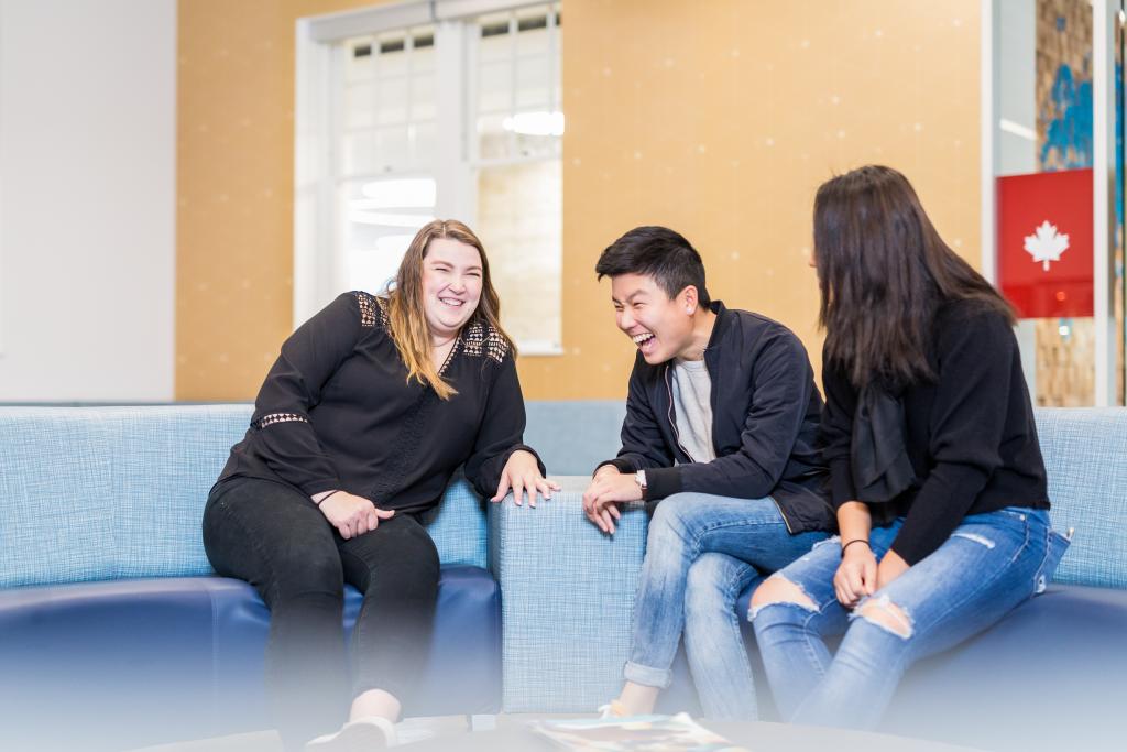 Three students laughing and chatting in the HUB inside the Sherman Jen Building.