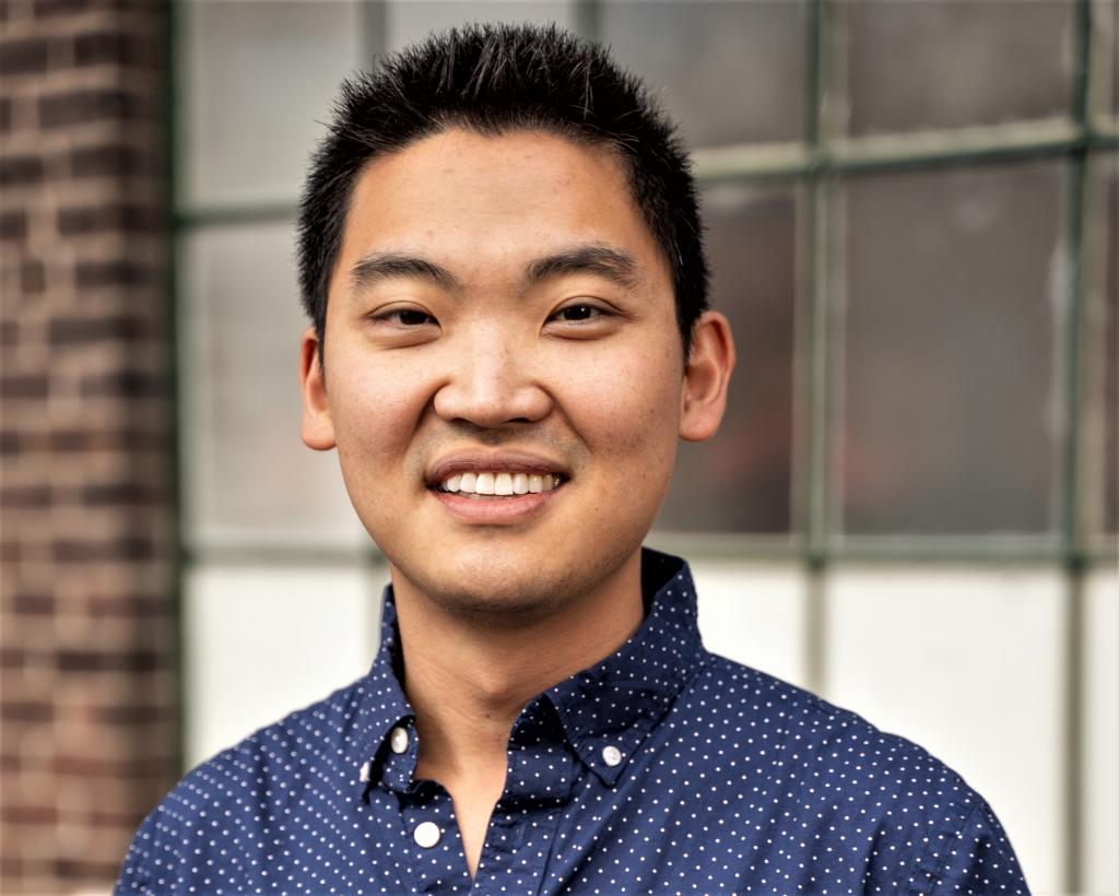 Man wearing blue collared shirt smiles at camera