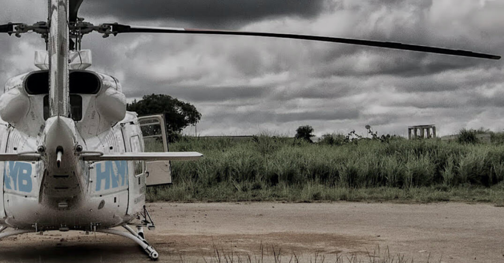 Helicopters Without Borders helicopter to the left on the ground and a field to the front and right on a cloudy day