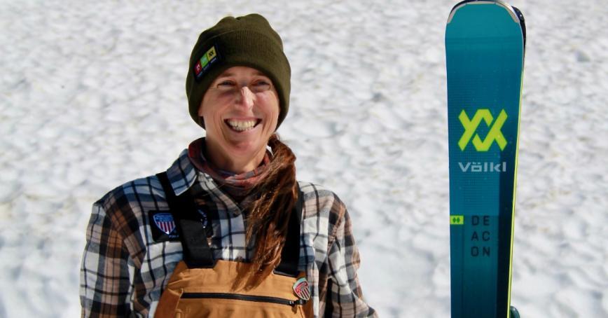 A woman poses on a snowy slope with skis.