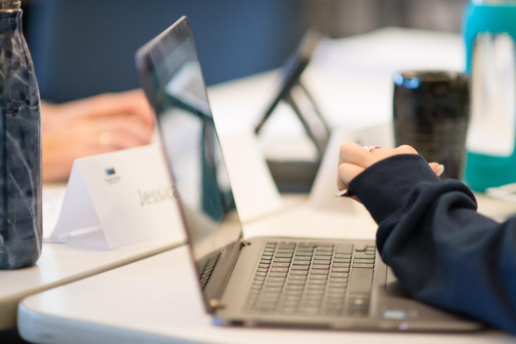 Close up of a Laptop and Students hands in a classroom setting