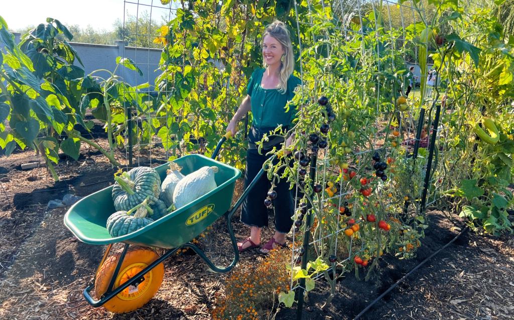 Solara Goodwynn pushing a wheelbarrow full of big squash through the Giving Garden.