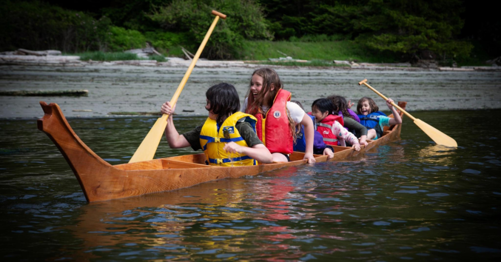 Children paddle in a dugout canoe.