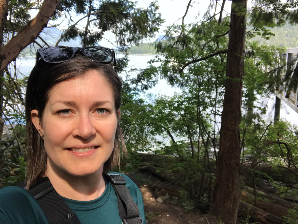 Caitlin Bingham smiling in front of a forest and lake