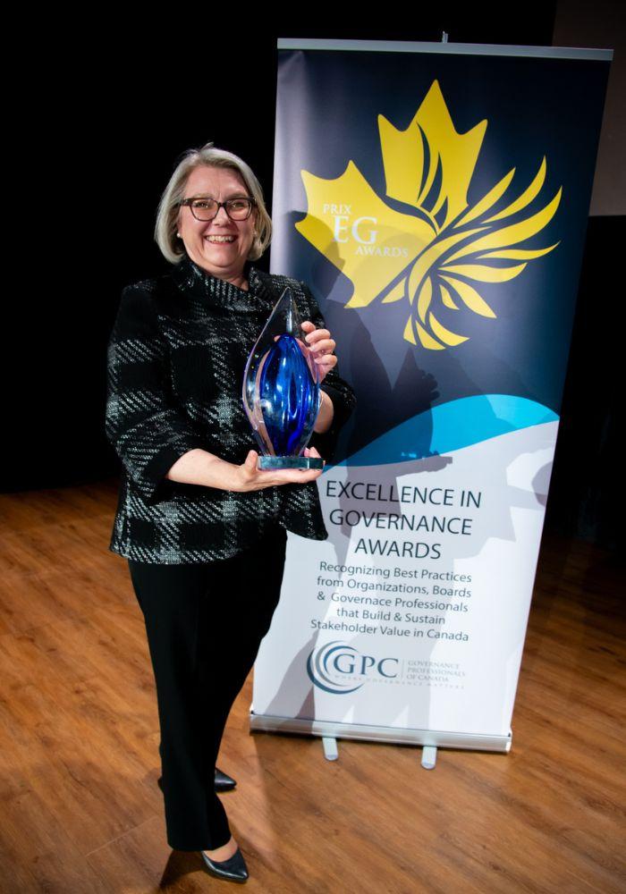 A woman smiles while holding a glass trophy.