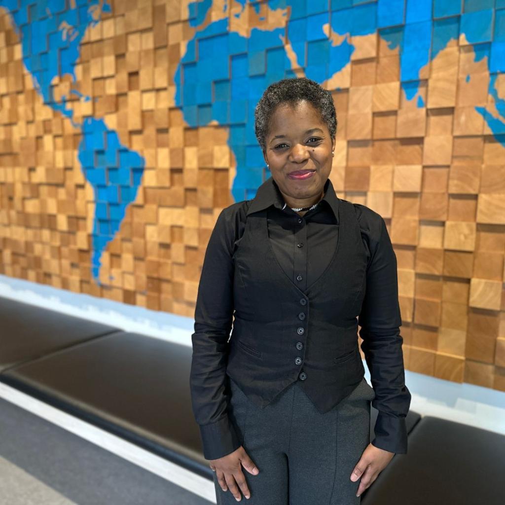 A woman smiles in front of a map of the world mural